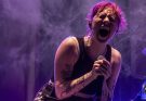 Vocalista de la banda Periferia cantando con energía en un concierto de punk-rock bajo luces moradas.