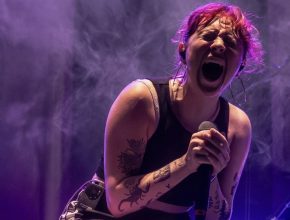 Vocalista de la banda Periferia cantando con energía en un concierto de punk-rock bajo luces moradas.