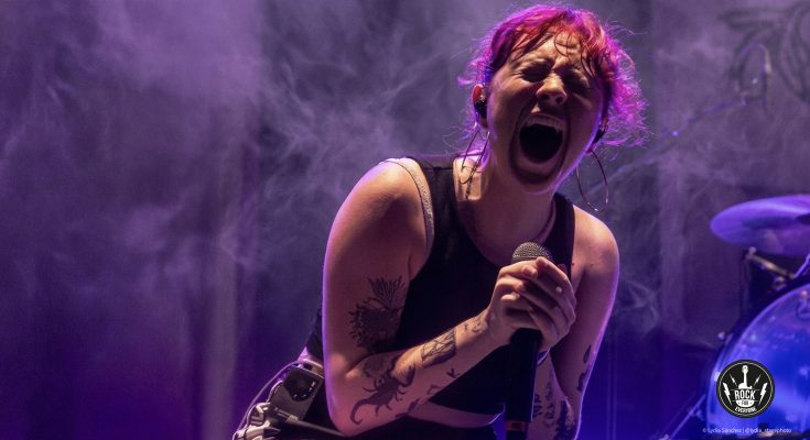 Vocalista de la banda Periferia cantando con energía en un concierto de punk-rock bajo luces moradas.